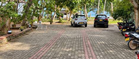 A paved pathway lined with trees and parked vehicles.