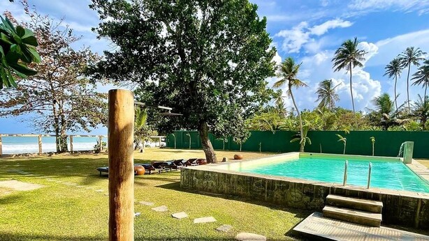 A swimming pool with a clear view of the ocean, surrounded by a grassy area and palm trees.