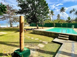 Piscina com vista clara para o oceano, rodeada por gramado e palmeiras.