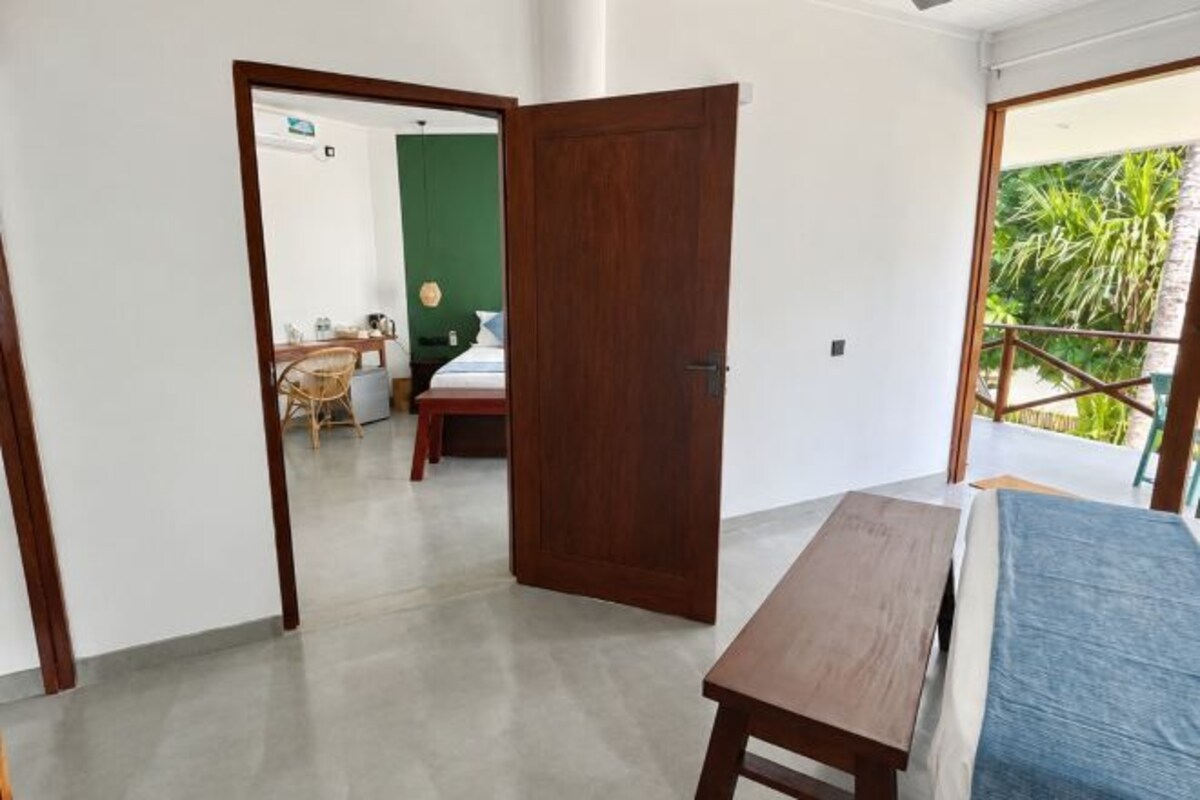 Una habitación con una cama, un banco de madera, una puerta que da a otra habitación y un balcón con vistas.
