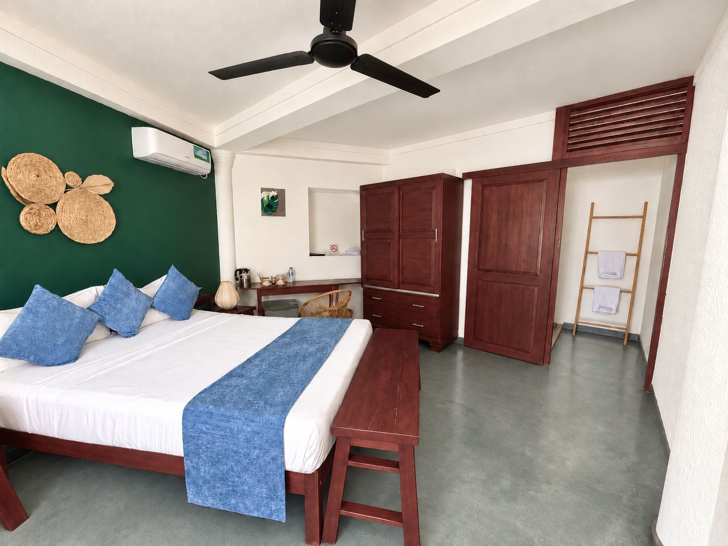 A hotel room with a bed, a desk, a wardrobe, and a ceiling fan.