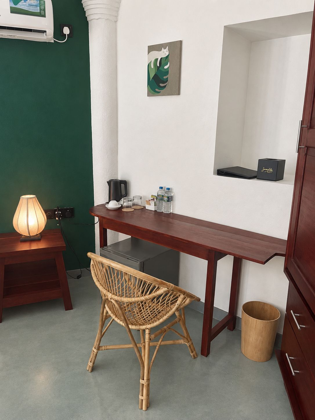 Habitación pequeña con escritorio, silla, lámpara y un cesto de basura.