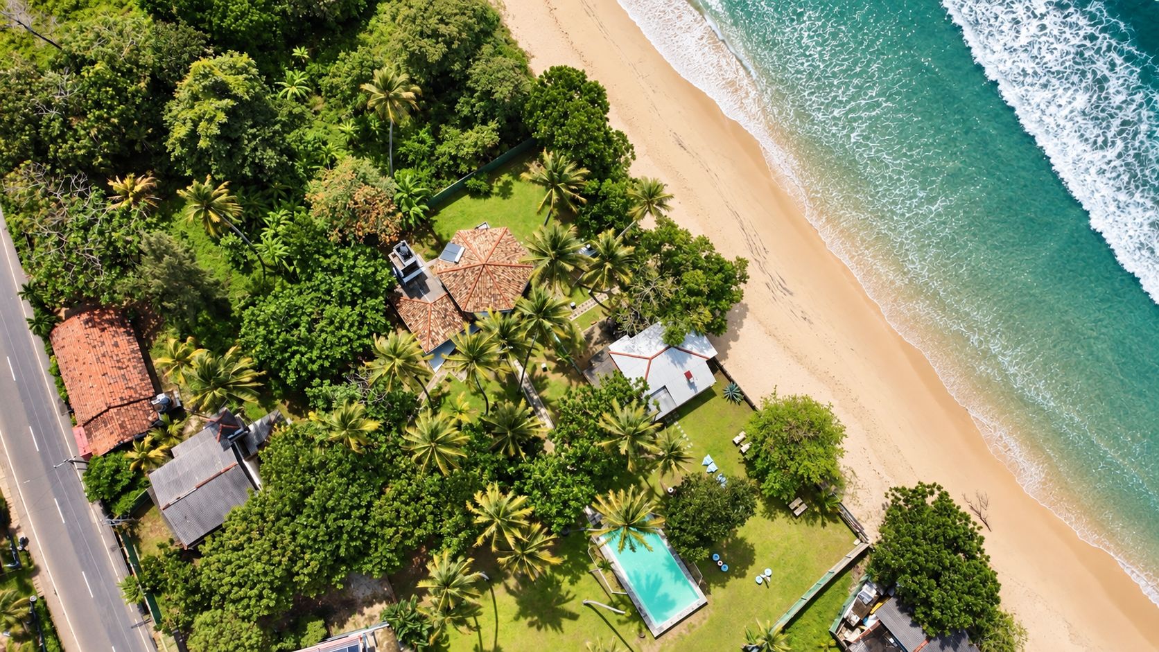 An aerial view of a coastal property with a swimming pool, beach access, and lush greenery.
