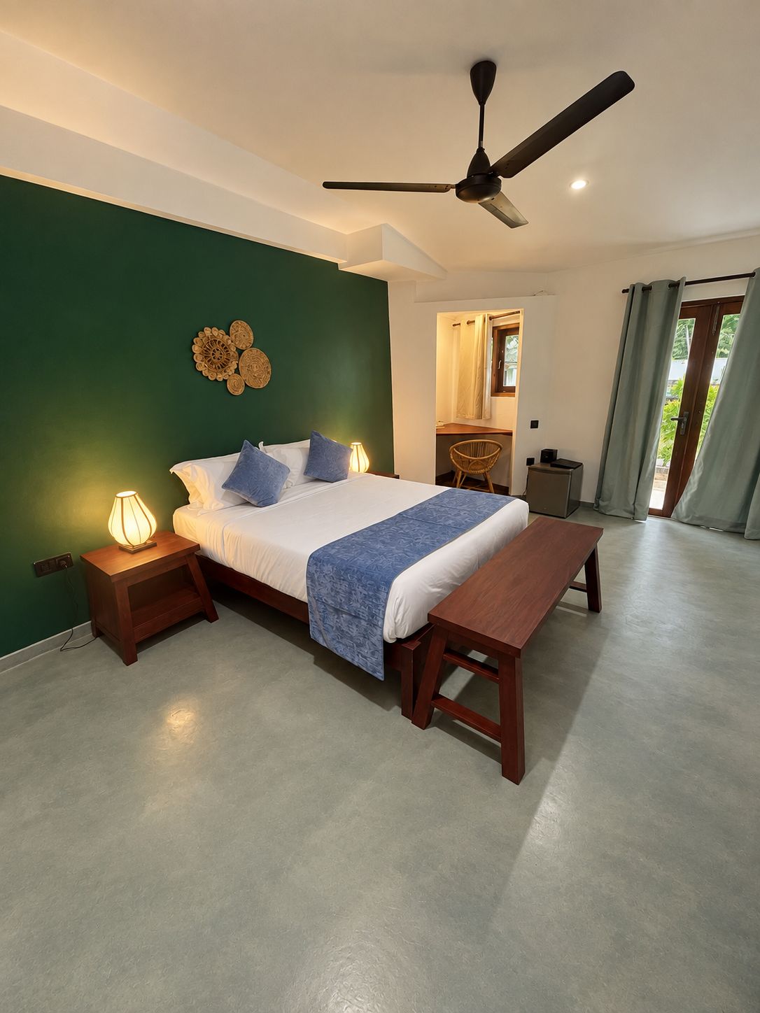 A bedroom with a bed, bedside tables, a ceiling fan, and a view of the outside.