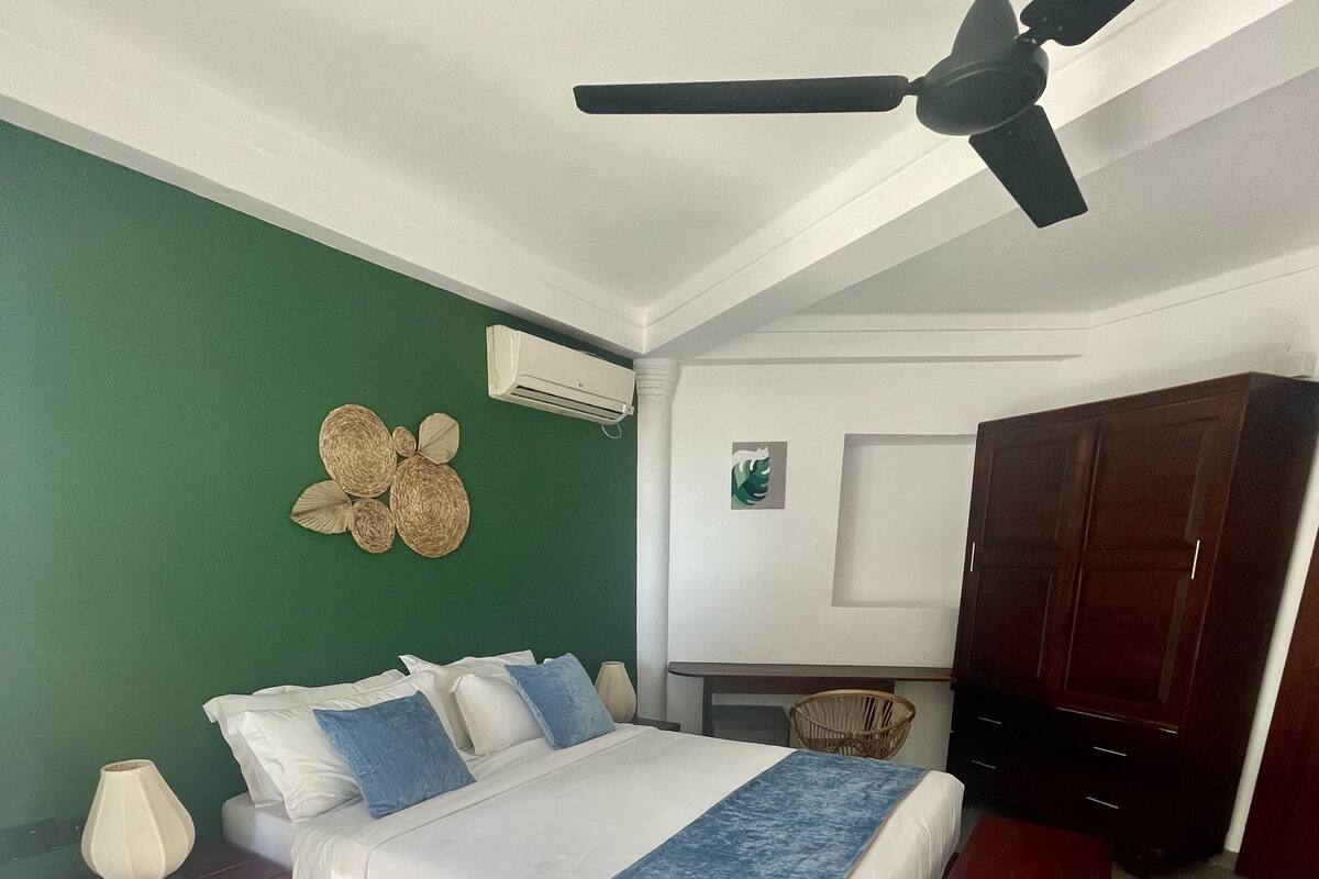 A bedroom with a bed, bedside tables, a ceiling fan, a wardrobe, and a wall-mounted air conditioner.