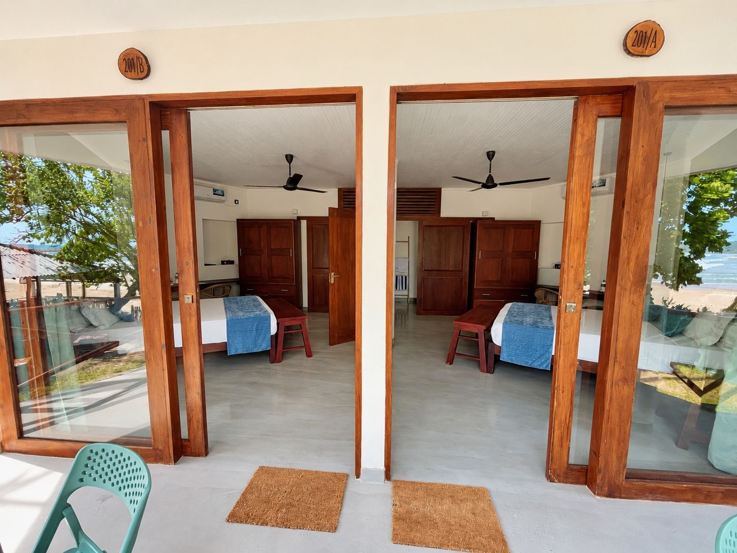 Quarto com cama, escrivaninha e cadeira, com vista para a praia através de uma porta de vidro.