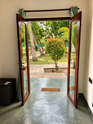 Puerta abierta que da a un patio con un árbol pequeño, un banco y suelo de baldosas.