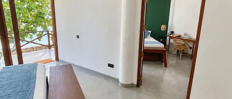 Habitación de hotel con cama, un banco de madera, ventilador de techo y vista al exterior.