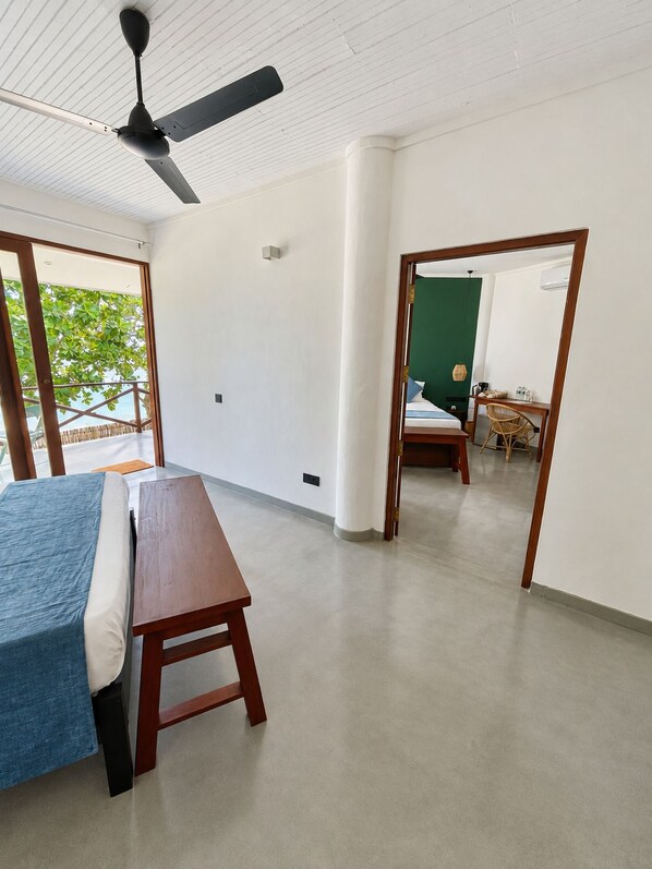 Habitación de hotel con cama, un banco de madera, ventilador de techo y vista al exterior.