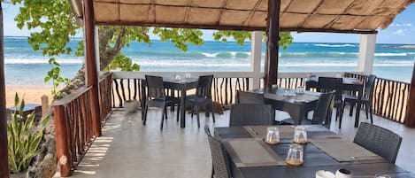 Un área de comedor exterior con mesas y sillas, con vista al océano.