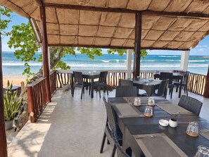 Un área de comedor exterior con mesas y sillas, con vista al océano.