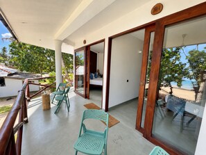 Un balcón con barandilla de madera, una cama con almohadones azules y vista a la playa.