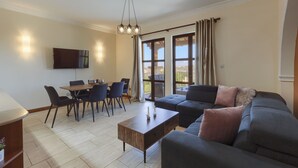 En moderne stue med sofa, sofabord, spisebord og stole. Der er et TV ophængt på væggen og et vindue med gardiner.