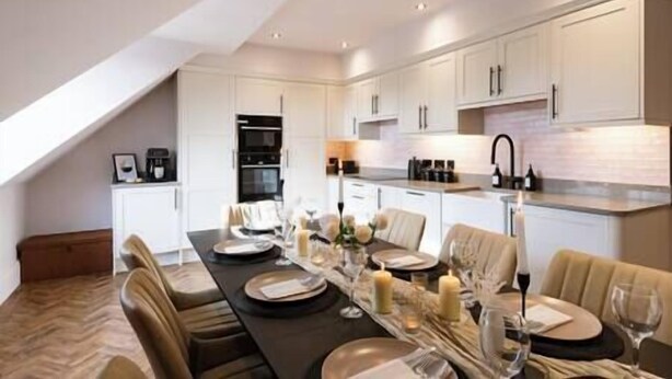A modern kitchen with white cabinetry, a dining area with a dark table set for six, and a visible oven. - Longshaw Loft - Family 3 Bed Apt WiFi & Parking (Buxton)