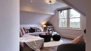 A cozy loft bedroom with a sloped ceiling, a large window, a bed, and a seating area with a sofa and a coffee table. - Longshaw Loft - Family 3 Bed Apt WiFi & Parking (Buxton)