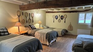 Quarto com três camas, vigas de madeira no teto e raquetes de tênis penduradas na parede.