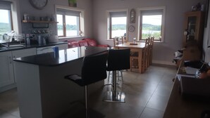A modern kitchen with a central island, dining area with wooden chairs, and large windows offering a view.