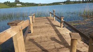 A wooden pier extending into a calm lake with grassy banks and houses in the background.