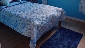 A bedroom with a bed, a window with a view of greenery, a vase with flowers, and a blue wall.
