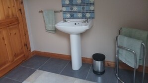 A bathroom with a white pedestal sink, a mirror above it, and a patterned tile backsplash.