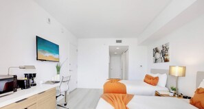 A hotel room with two beds, a desk with a coffee maker, a TV, and artwork on the walls.