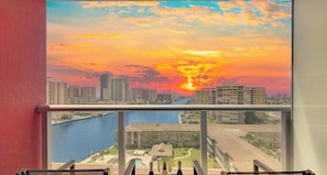 Un balcón con vista a la ciudad al atardecer, incluyendo edificios altos y un puerto deportivo.