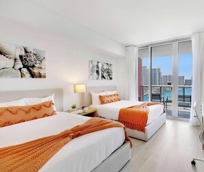 Habitación de hotel con dos camas, un escritorio, una silla, vista a la ciudad y obras de arte en las paredes.