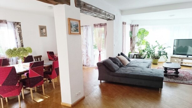 Un salon avec un canapé gris, un plancher en bois et un coin repas avec des chaises rouges et noires.