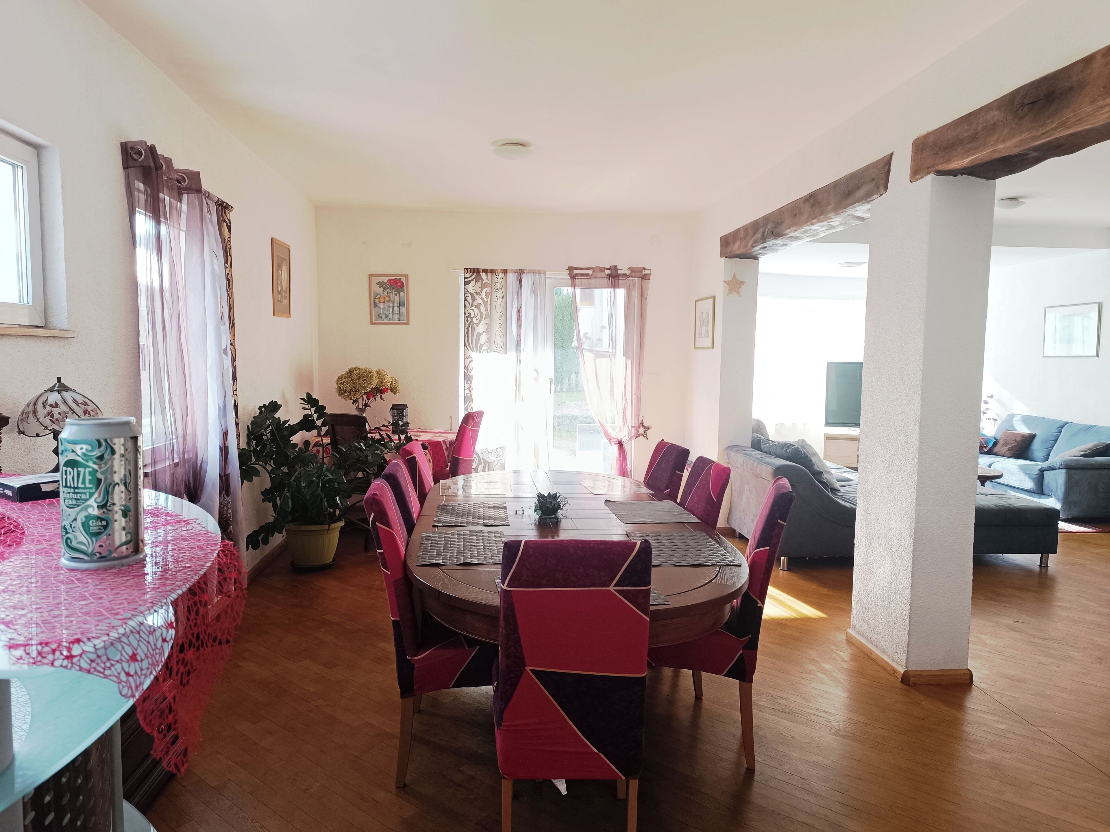 A dining area with a round table, red and black chairs, and a pink tablecloth. There is a plant on the table and a can of drink on the side.
