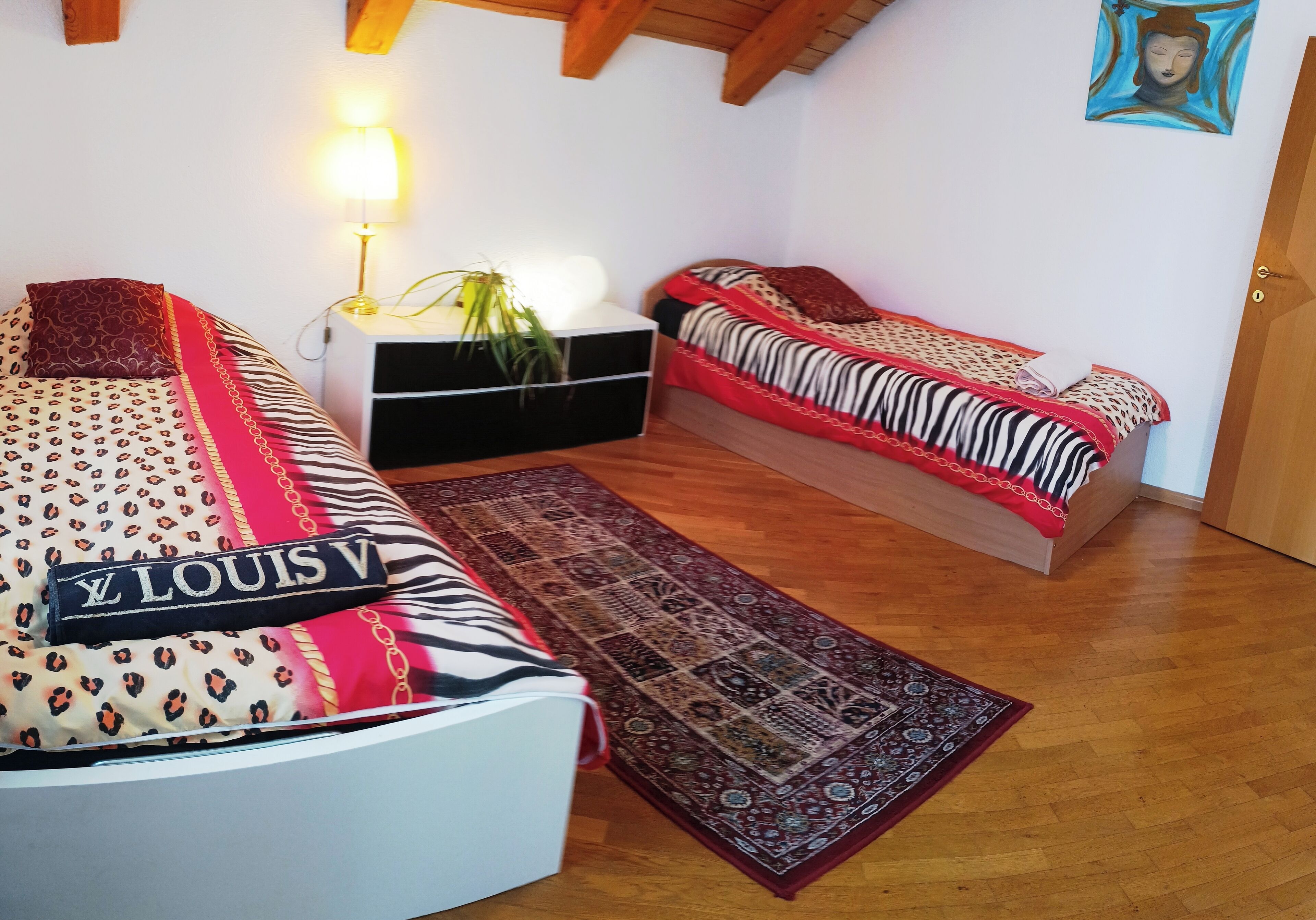 Une chambre avec deux lits, une table de chevet avec une lampe, une plante et un tapis à motifs.