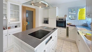 Une cuisine moderne avec des meubles blancs, une cuisinière encastrée et un garde-manger doté de portes en verre.