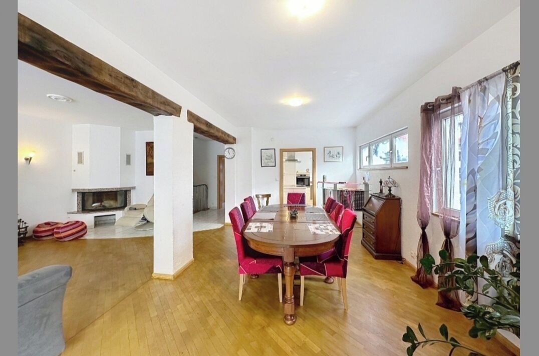 Ein Essbereich mit Holztisch, roten Stühlen, Kamin und Blick ins Freie.