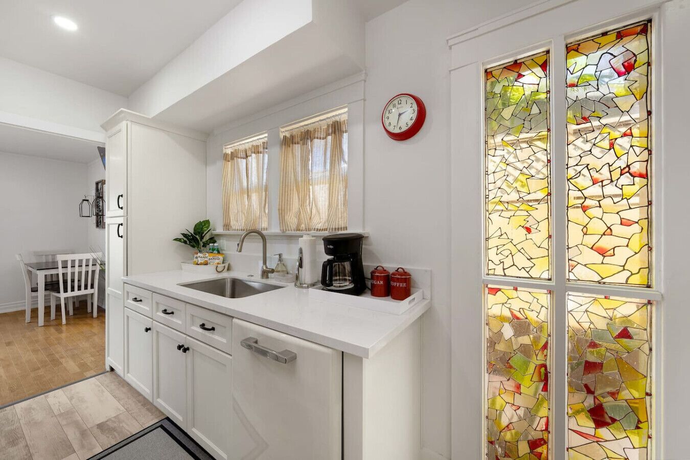 A modern kitchen with white cabinetry, a double sink, a coffee maker, and a clock on the wall.