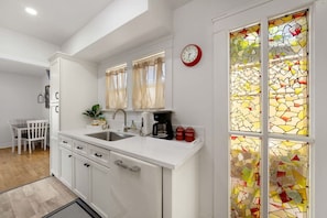 A modern kitchen with white cabinetry, a double sink, a coffee maker, and a clock on the wall.