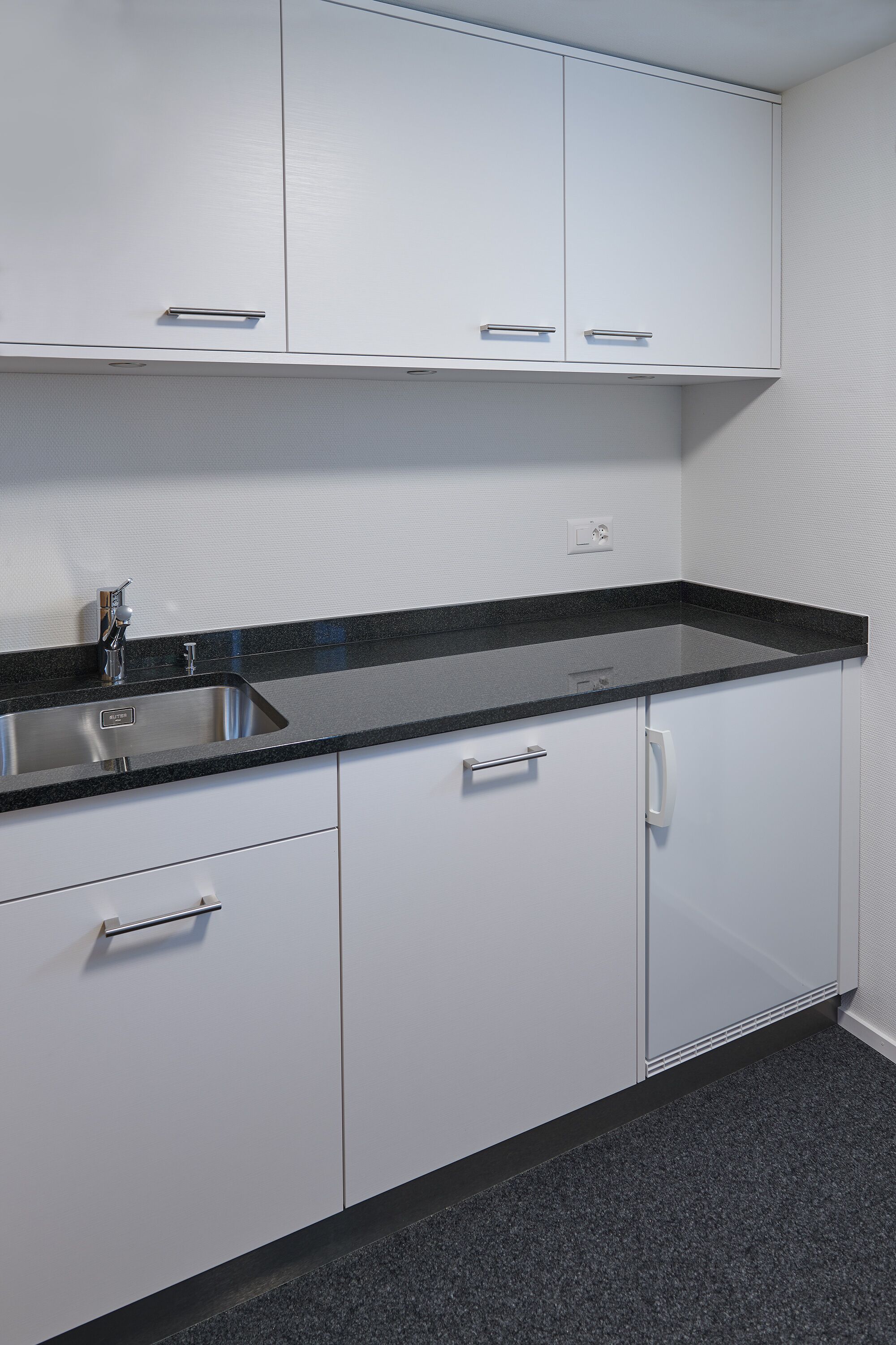 A kitchen with white cabinets, a black countertop, and a stainless steel sink.