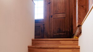 Eine Holztreppe führt zu einem Raum mit einer Holztür und einem Fenster.