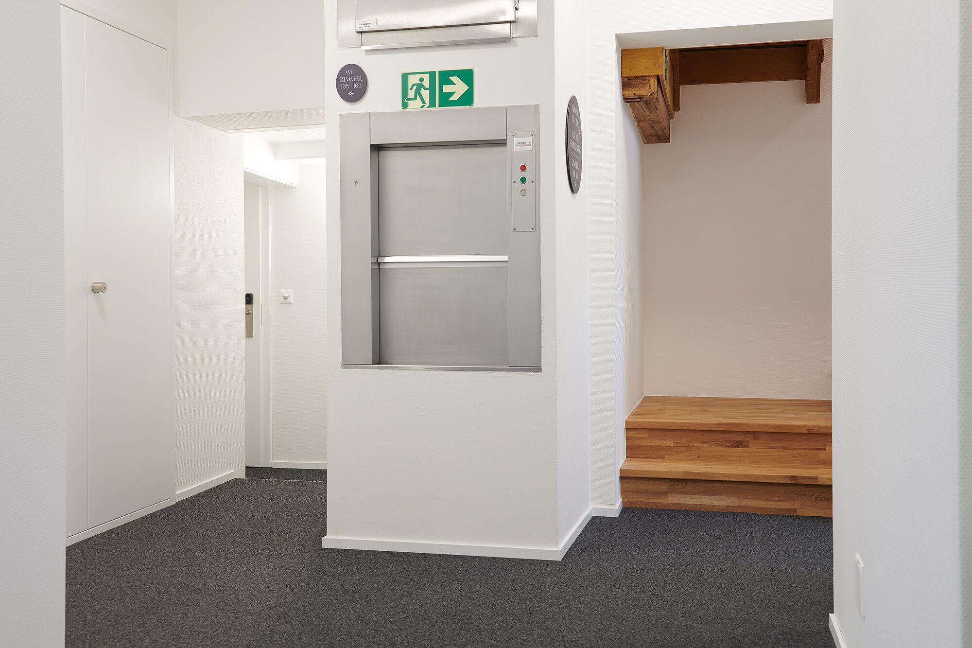 A hallway with a white door, a fire alarm, and a staircase with wooden steps.