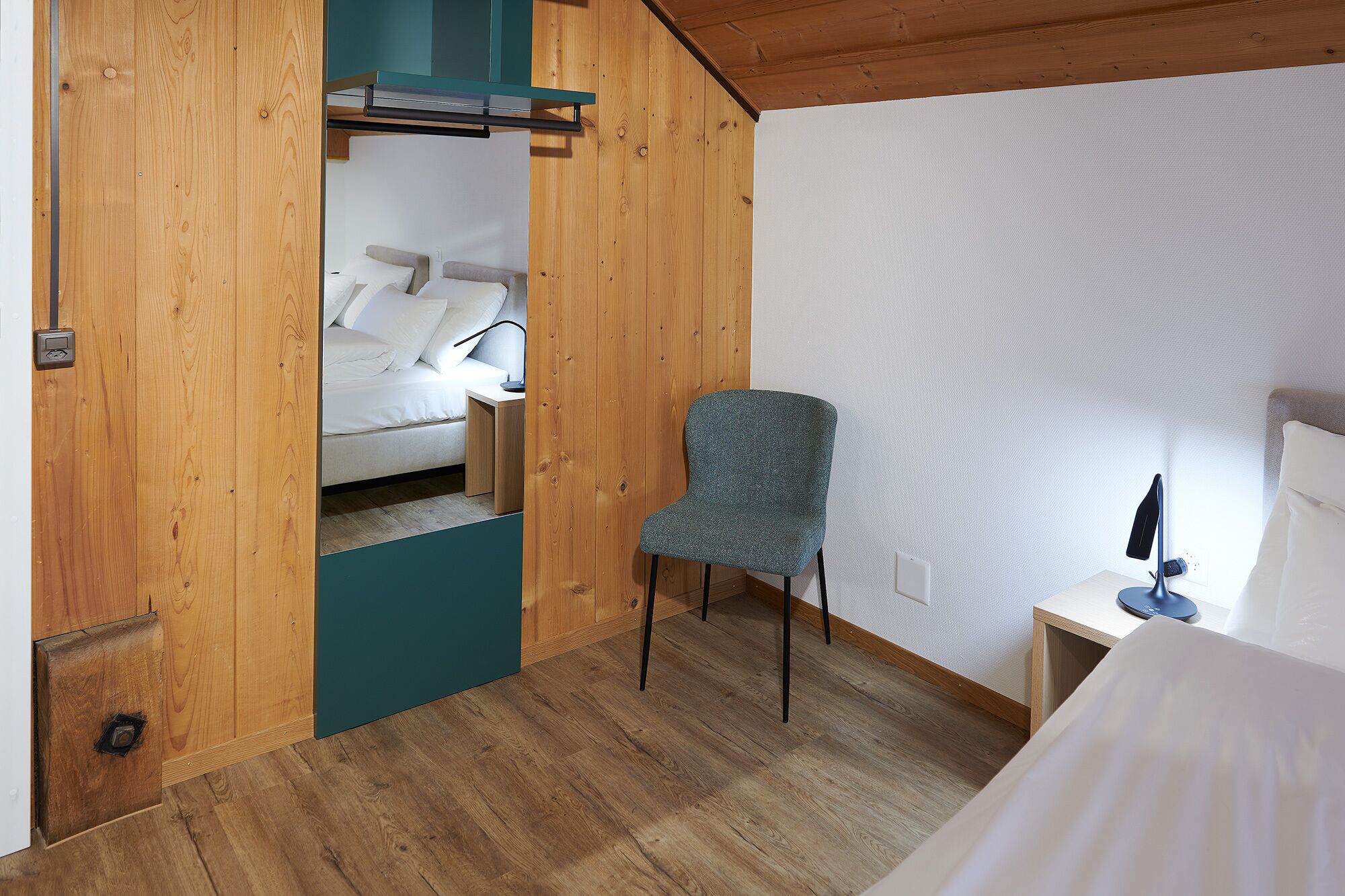 A bedroom with a bed, a chair, and a desk with a lamp.