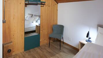 A bedroom with a bed, a chair, and a desk with a lamp.