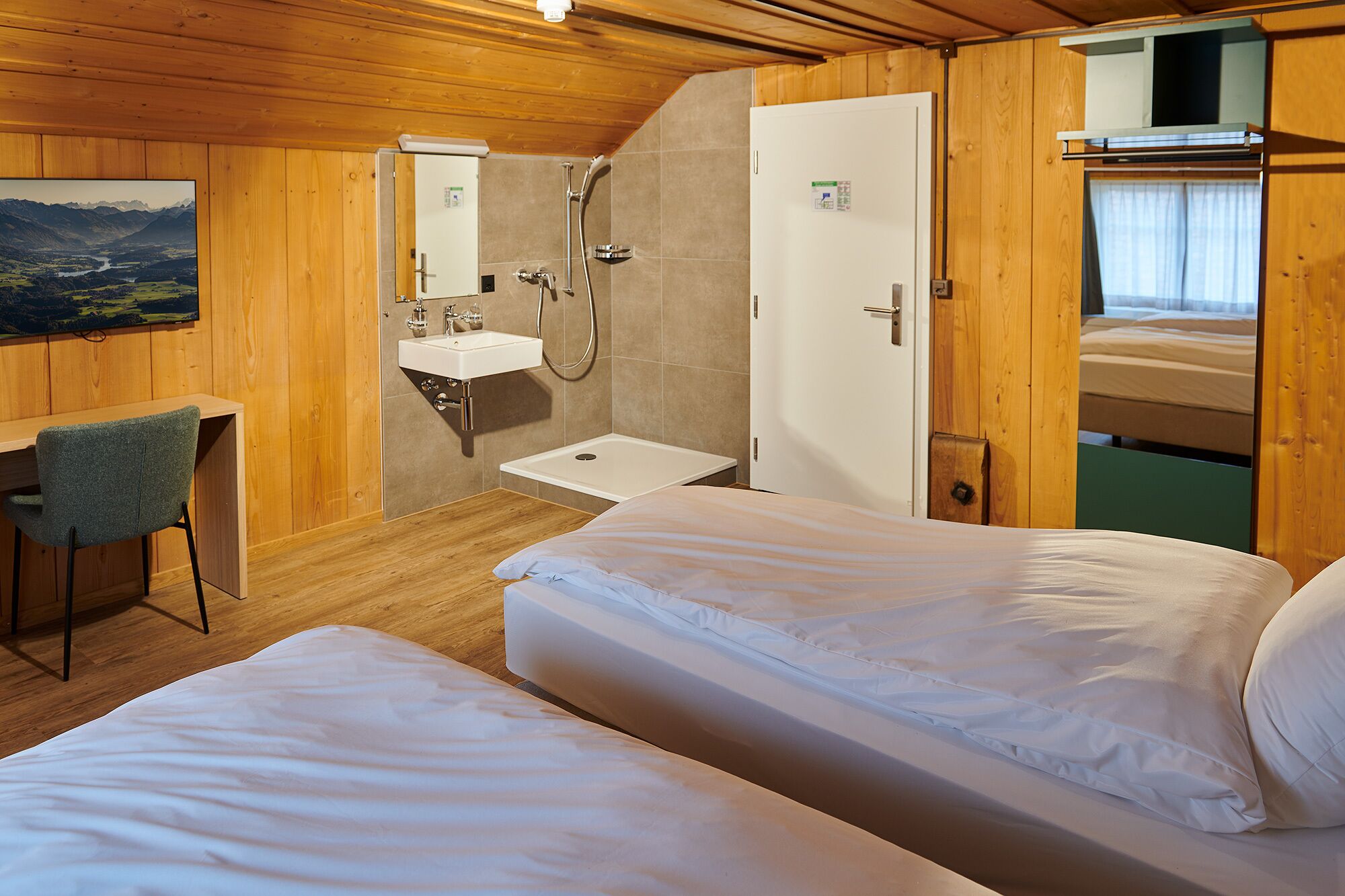 A room with two beds, a desk, a sink, and a shower.