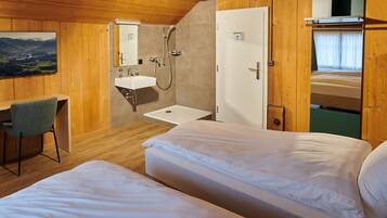 A room with two beds, a desk, a sink, and a shower.