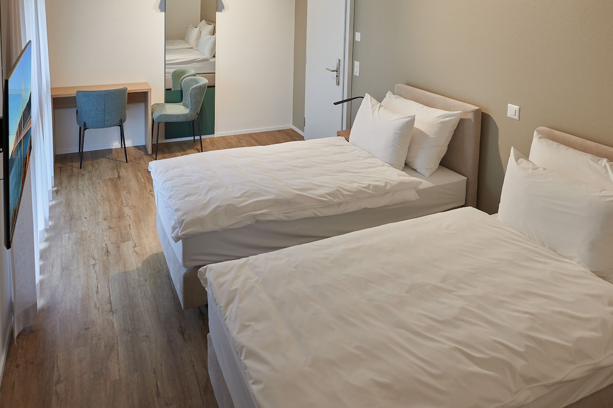 A hotel room with two beds, a desk, and a chair.