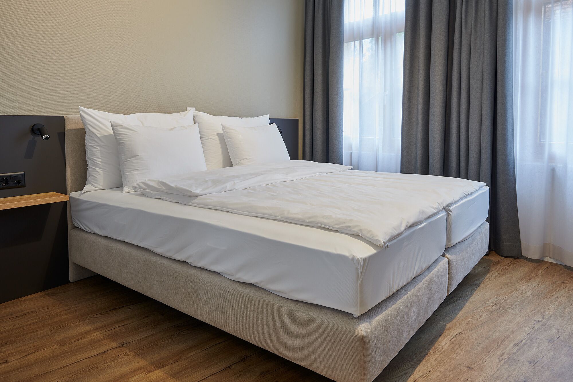 A neatly made bed with white linens in a modern hotel room.