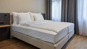 A neatly made bed with white linens in a modern hotel room.