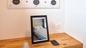 A hotel room with a bed, a bedside table, a charging station, and a QR code for check-in and check-out.