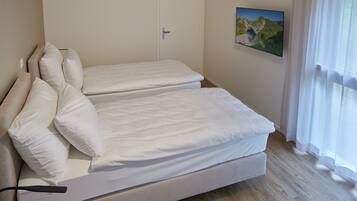 A bedroom with two single beds, a wooden floor, a door, and a window with curtains.