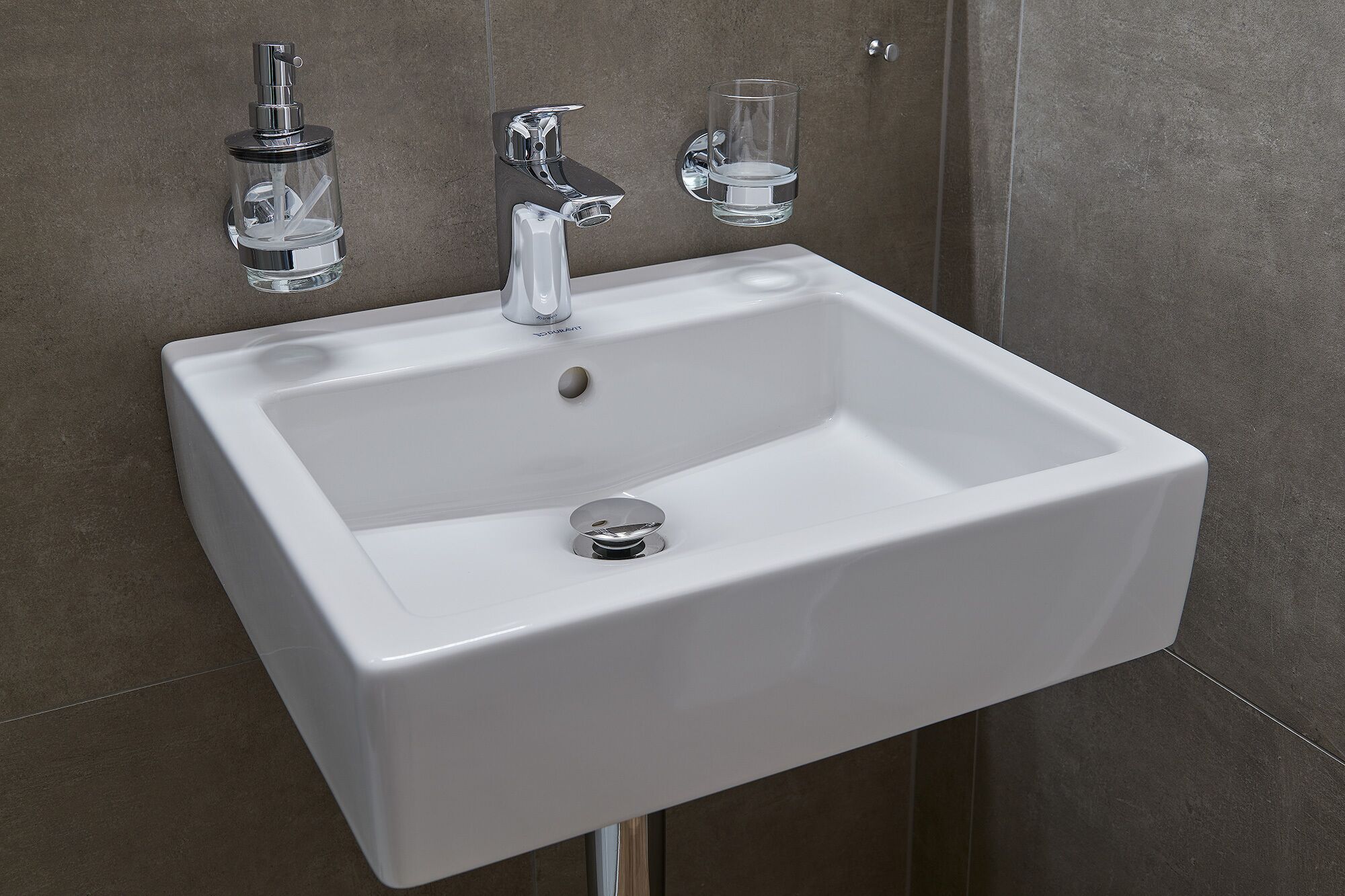 A white bathroom sink with a chrome faucet and a glass soap dispenser.