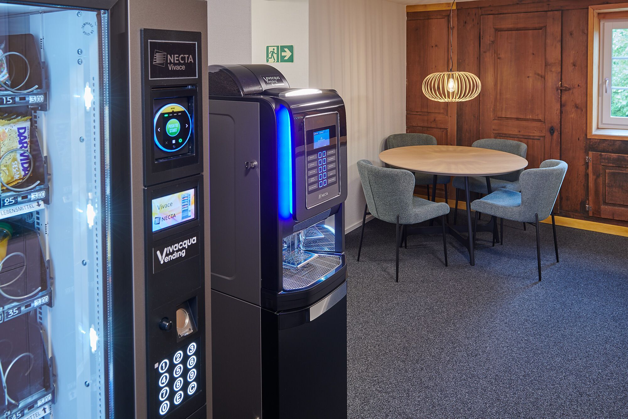 A vending machine with a digital display and a keypad, a small table with chairs, and a wooden door in the background.