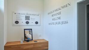 Ein Hotelrezeptionsbereich mit einem Holzbalken, einem Check-in-Schild, einem QR-Code und einem Willkommensschild.