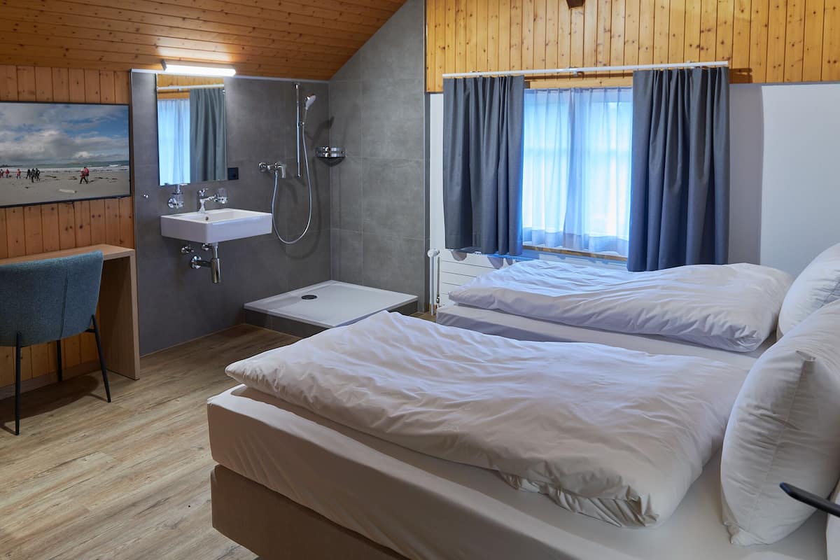 A room with two beds, a sink, and a shower.